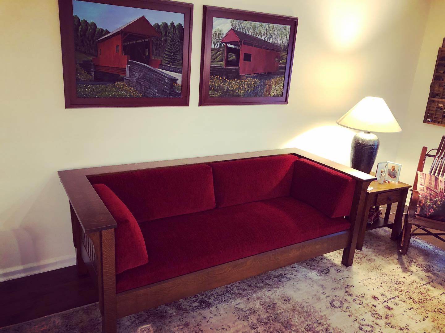 Red couch in a living room beside a lamp and side table, with two framed photos above and a patterned rug.
