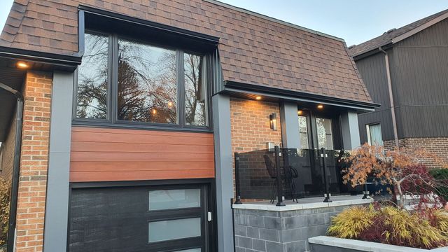 A brick house with a brown roof and a black garage door.