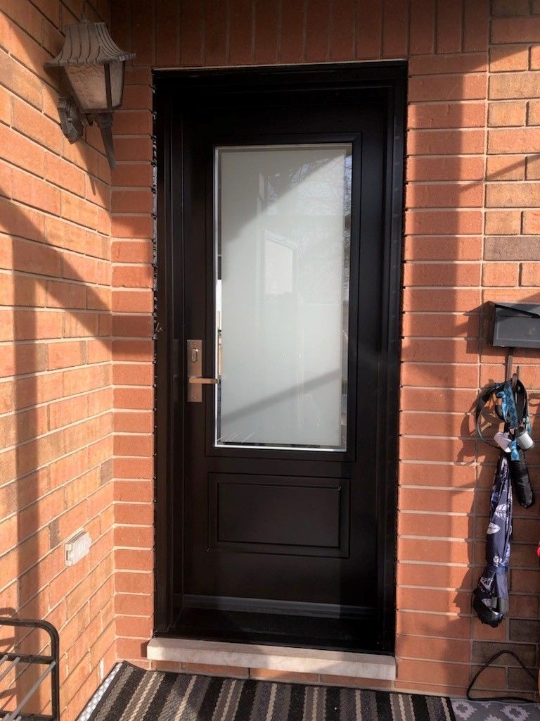 A black door with a glass window is on a brick wall.