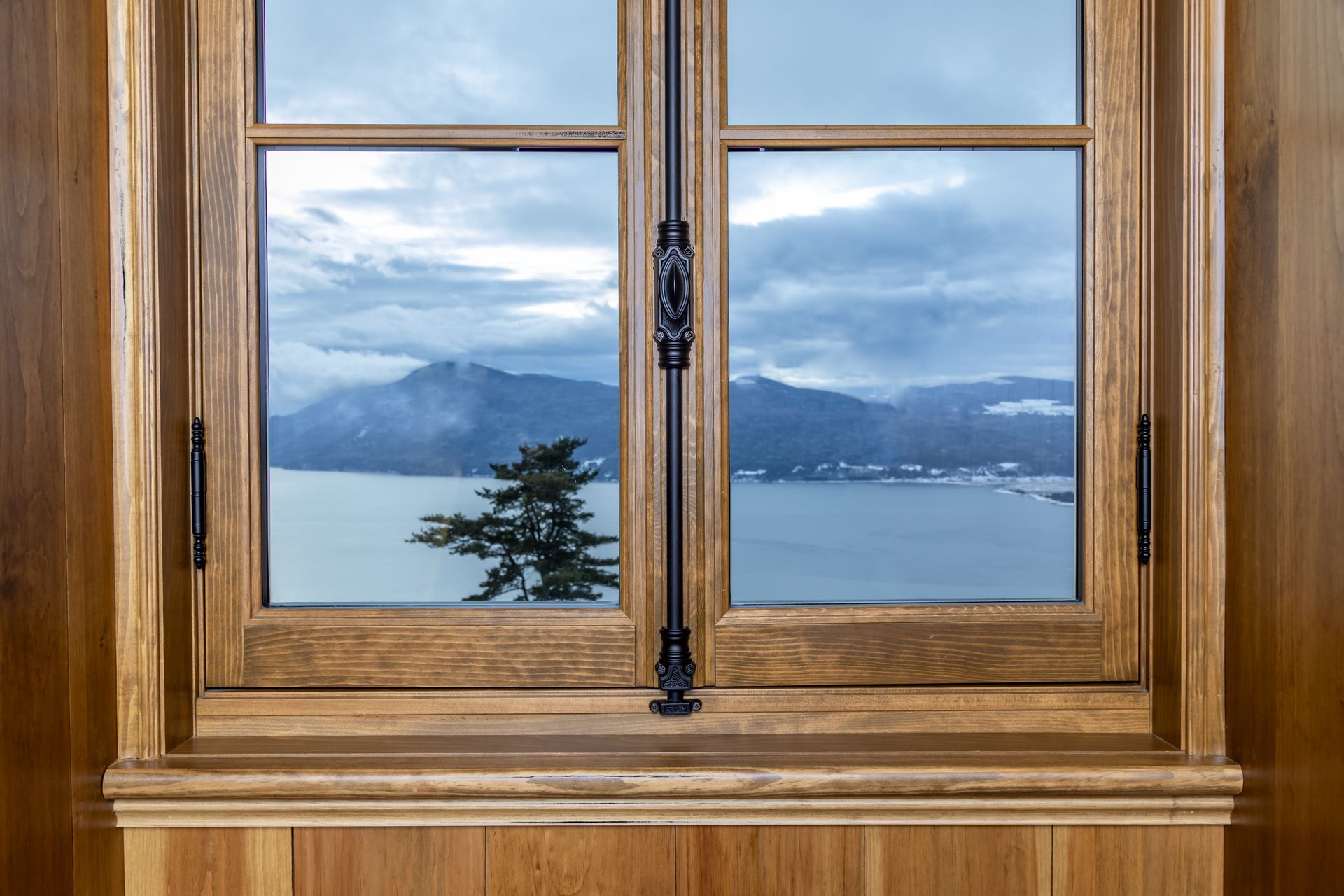 A wooden window with a view of a lake and mountains.