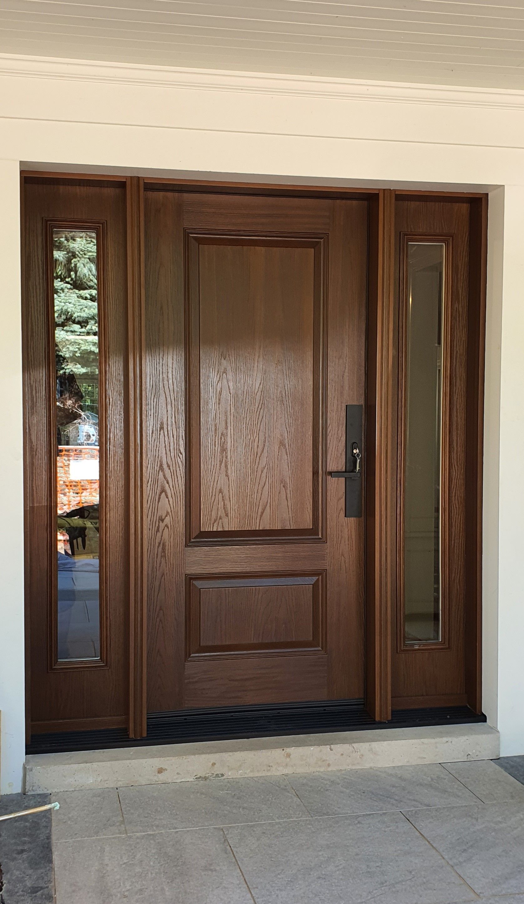 A large wooden door with two windows is sitting on a porch.