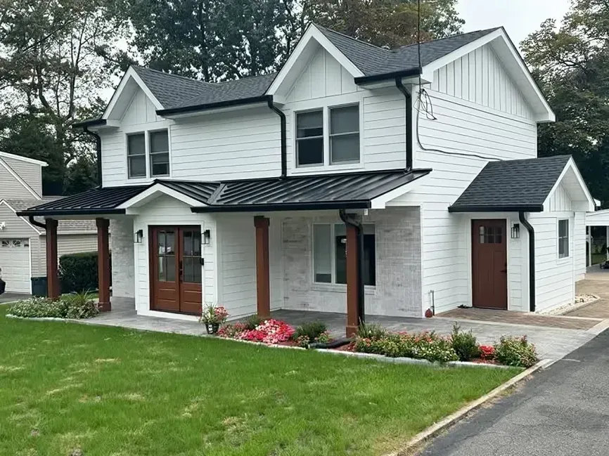 White two-story house with dark roof, brick porch, and a green front lawn