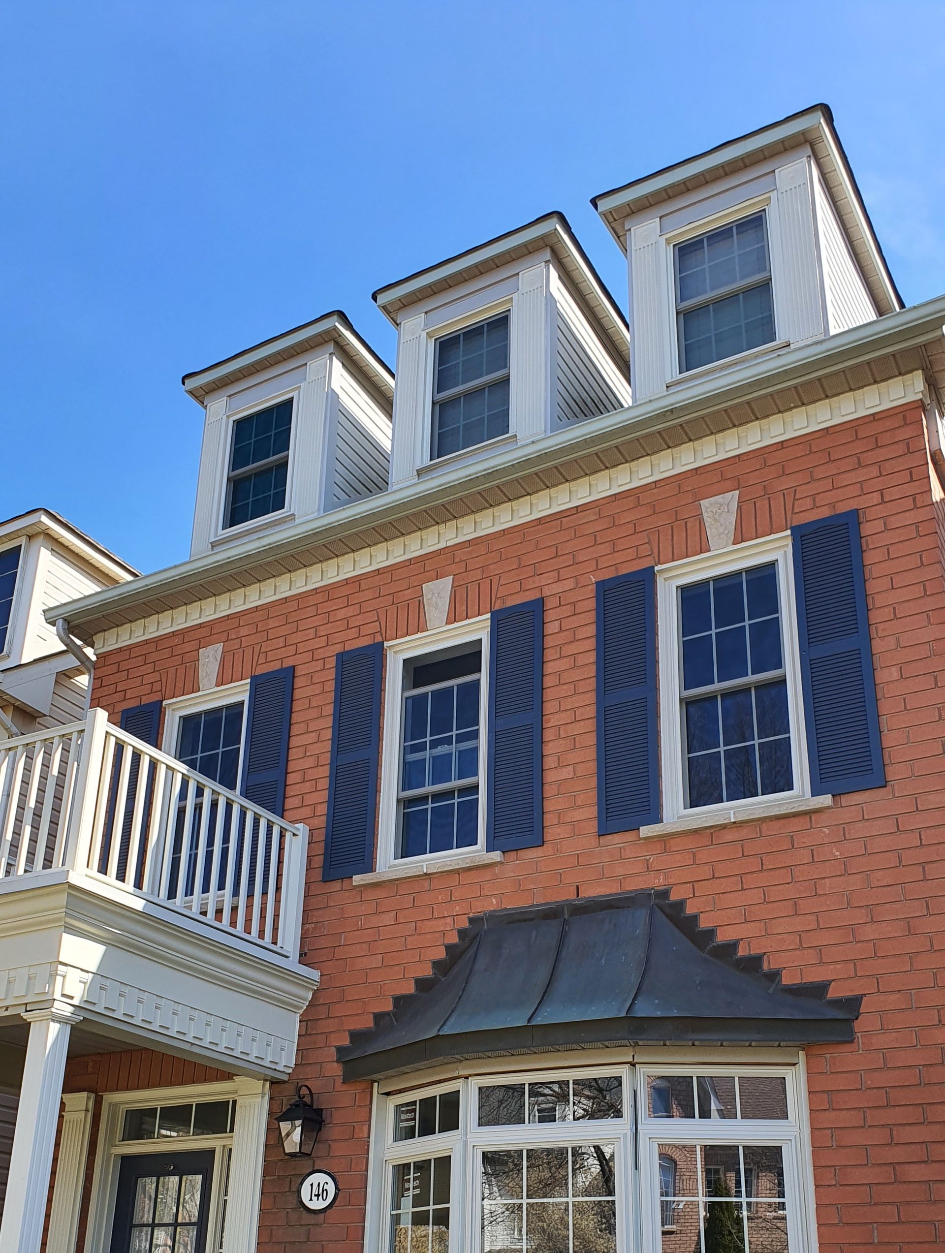Red brick townhouse with blue shutters, white trim, and dormer windows under a clear blue sky