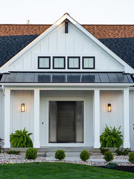Modern white house front entrance with black roof, central doorway, and potted greenery