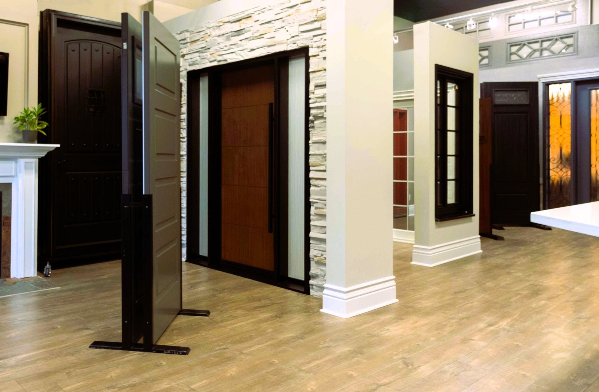 Modern showroom with wood flooring, stone walls, and several display door samples.