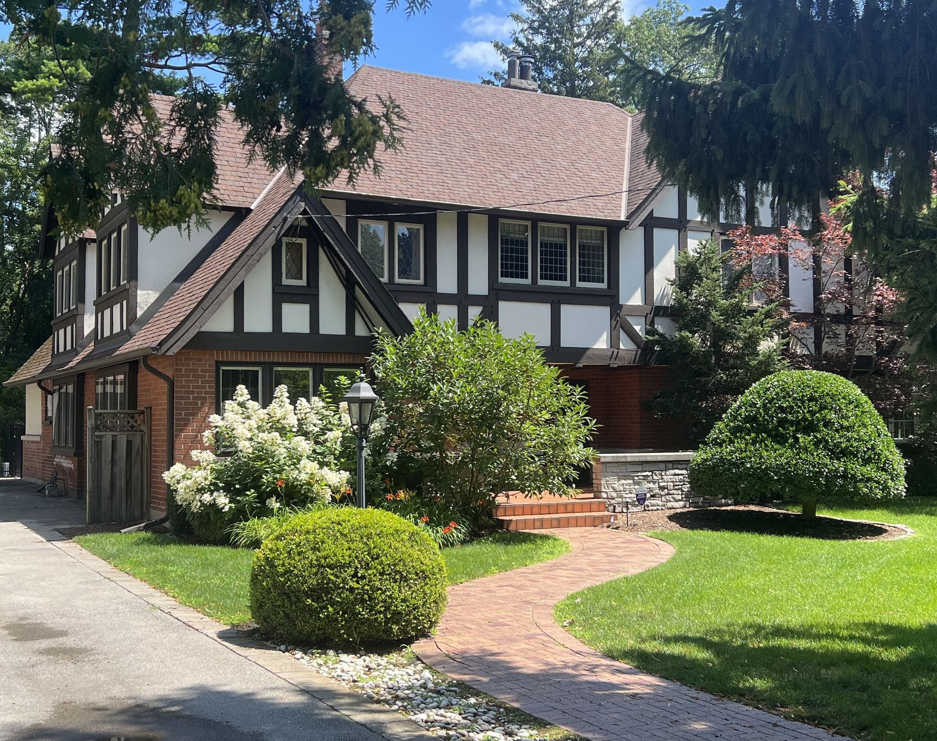 A two-story Tudor-style home with white stucco, dark timber framing, a brown roof, and a red brick path leading to the door.