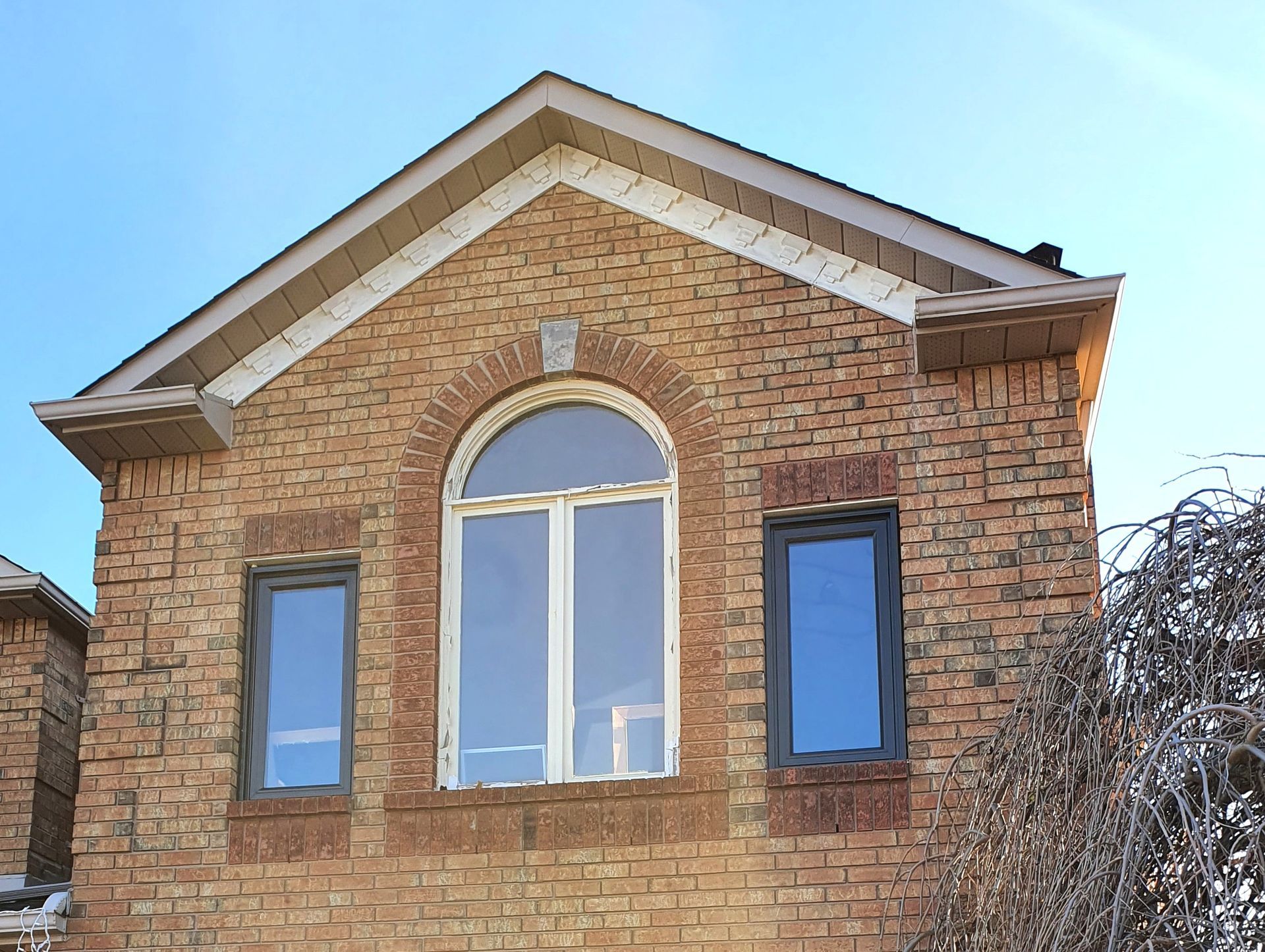 Brick house facade with arched central window and two blue side windows under a peaked roof