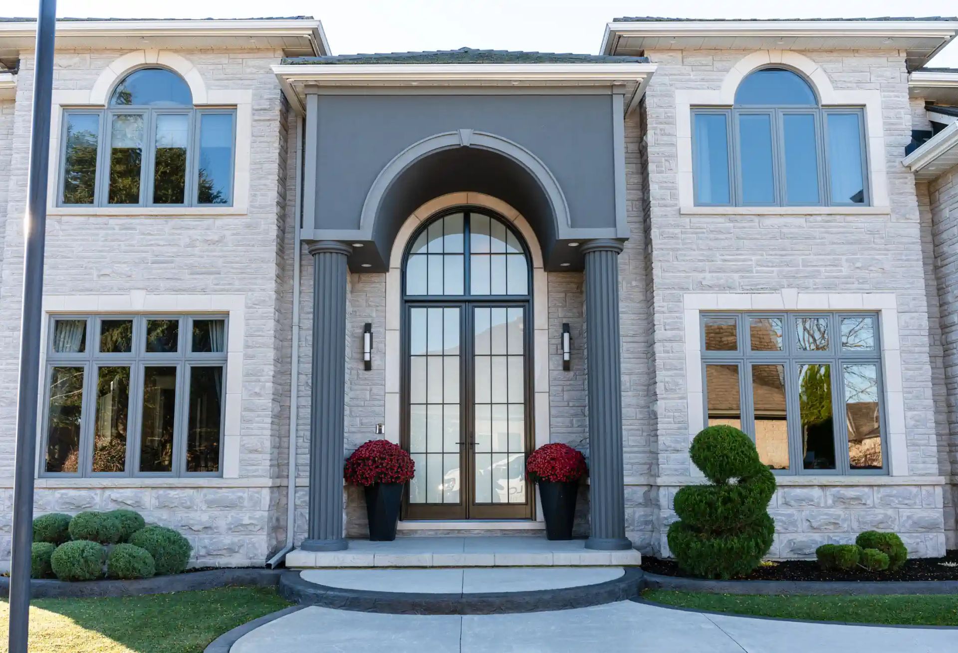 Grand stone mansion with arched entry, large windows, and red potted plants at the front door