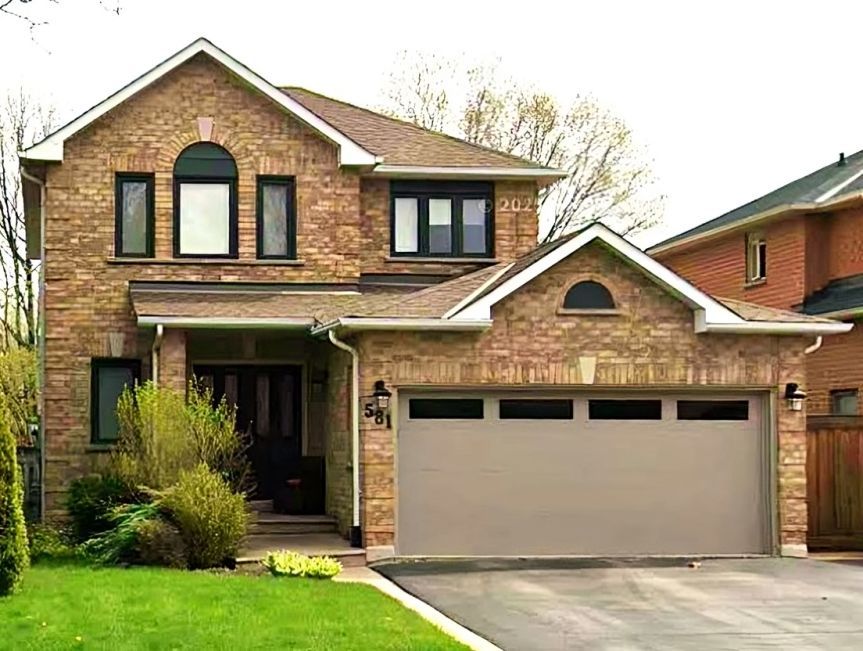 Two-story brick house with beige garage door and green lawn in a suburban neighborhood