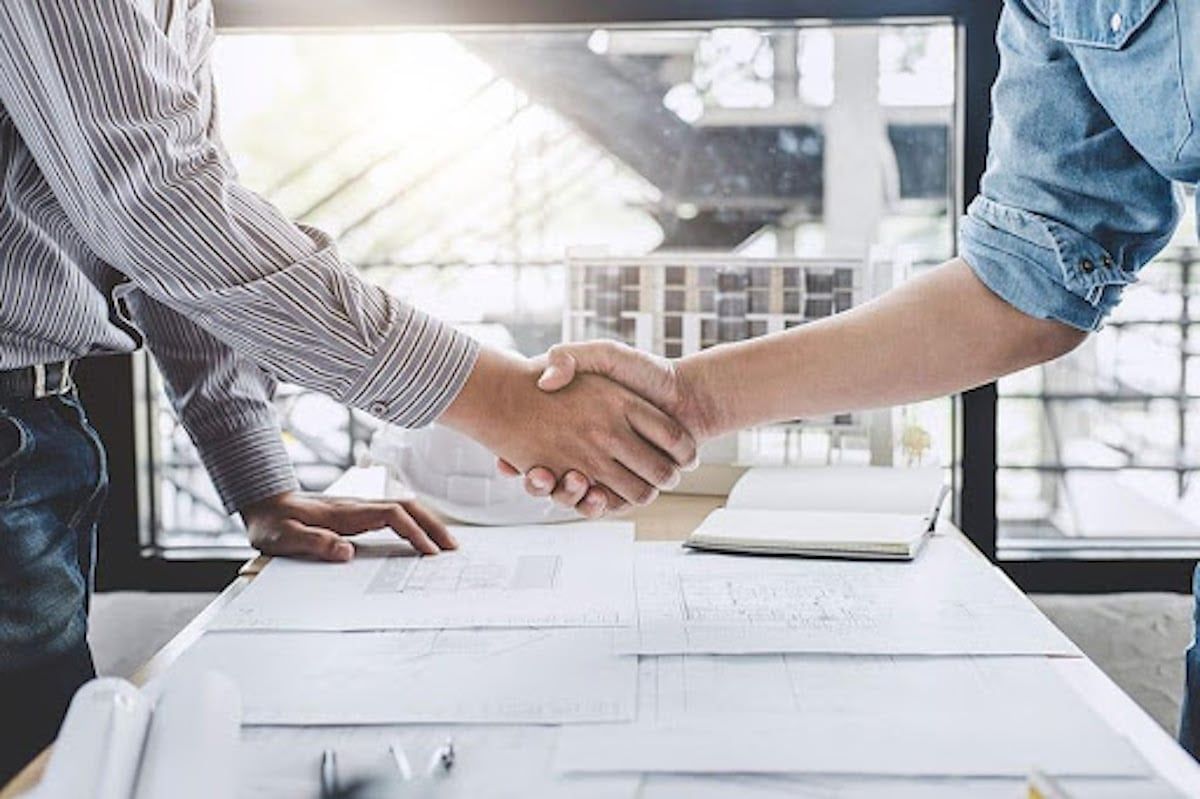 Two men are shaking hands over a table.