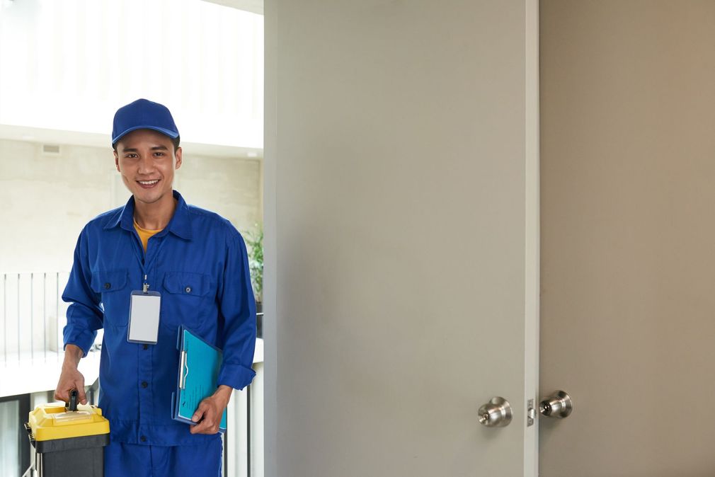 A man in a blue uniform is holding a vacuum cleaner and a clipboard.