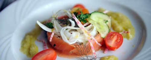 Une assiette blanche garnie d'une salade de tomates, concombres, oignons et moutarde.