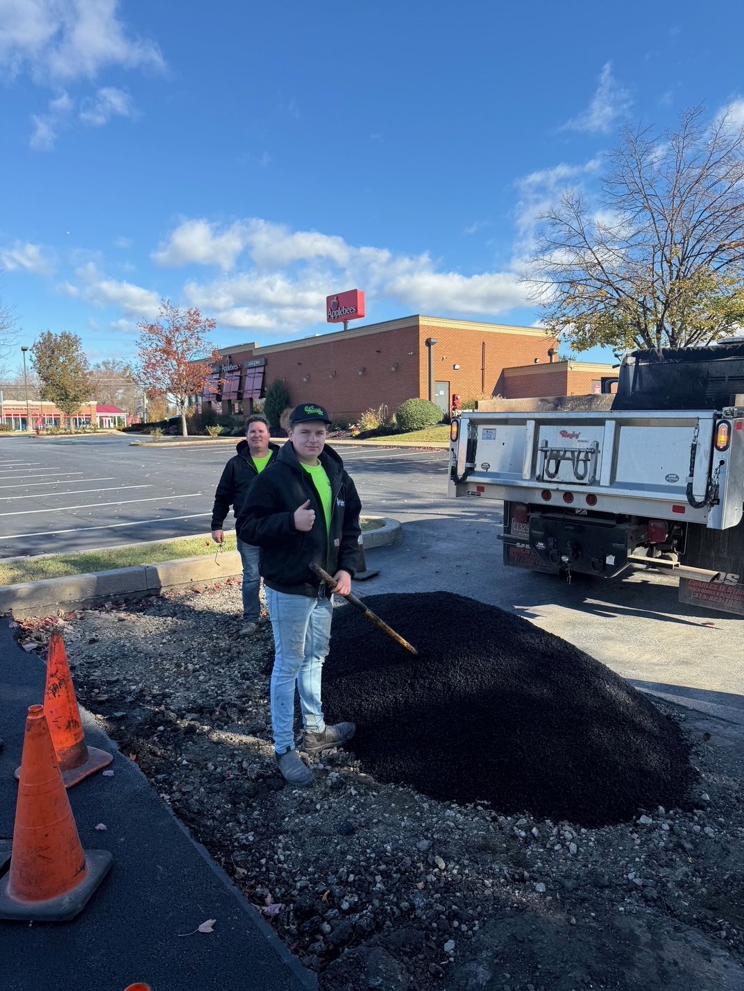 Two Men Are Standing Next to A Dump Truck in A Parking Lot.