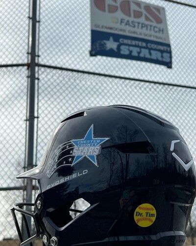 Black football helmet with blue star decals in front of a chain-link fence and stadium sign.