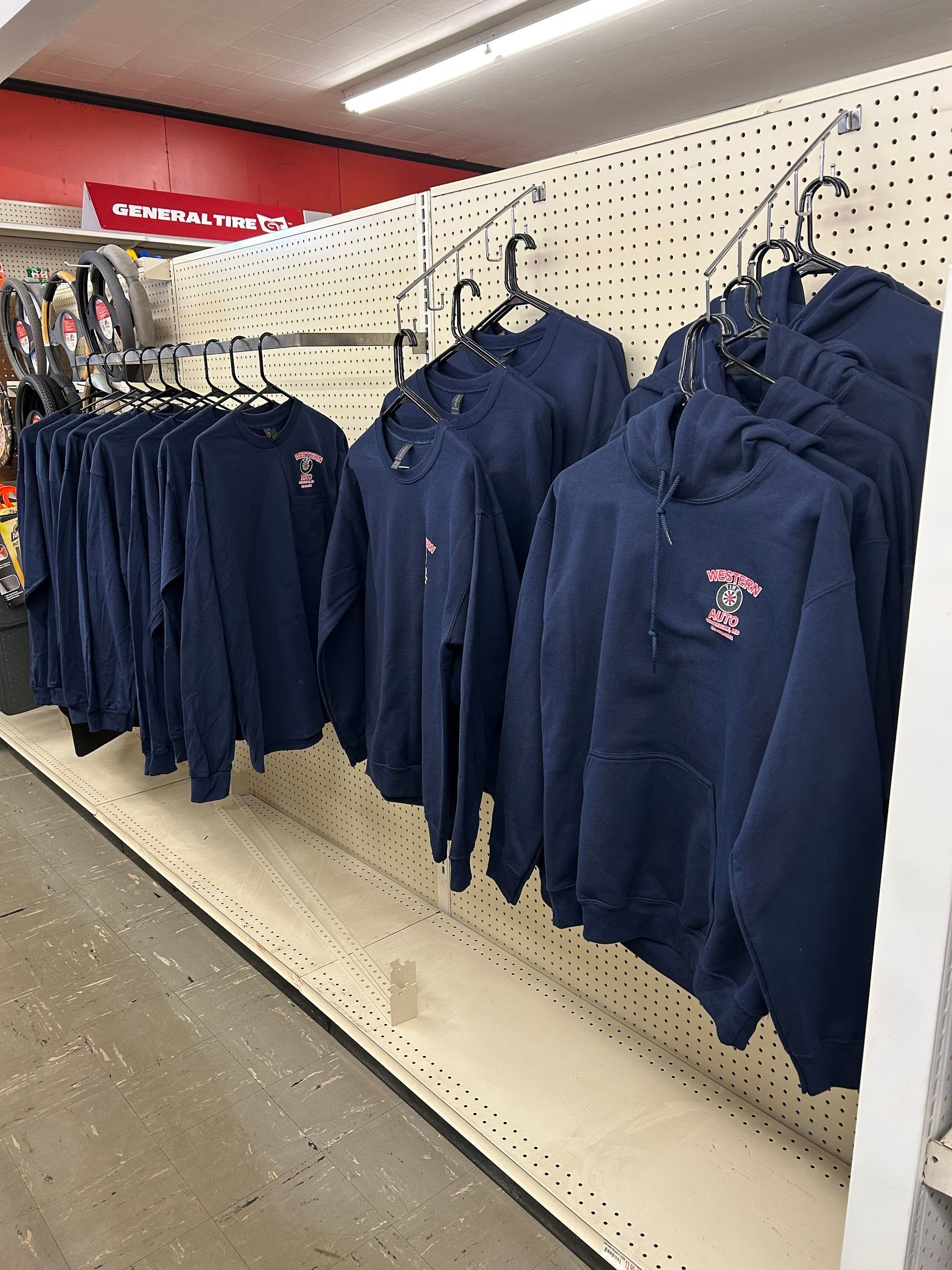 Apparel on hangers: navy blue sweatshirts and hoodies with a small logo; retail store setting | Western Tire & Auto of Centreville