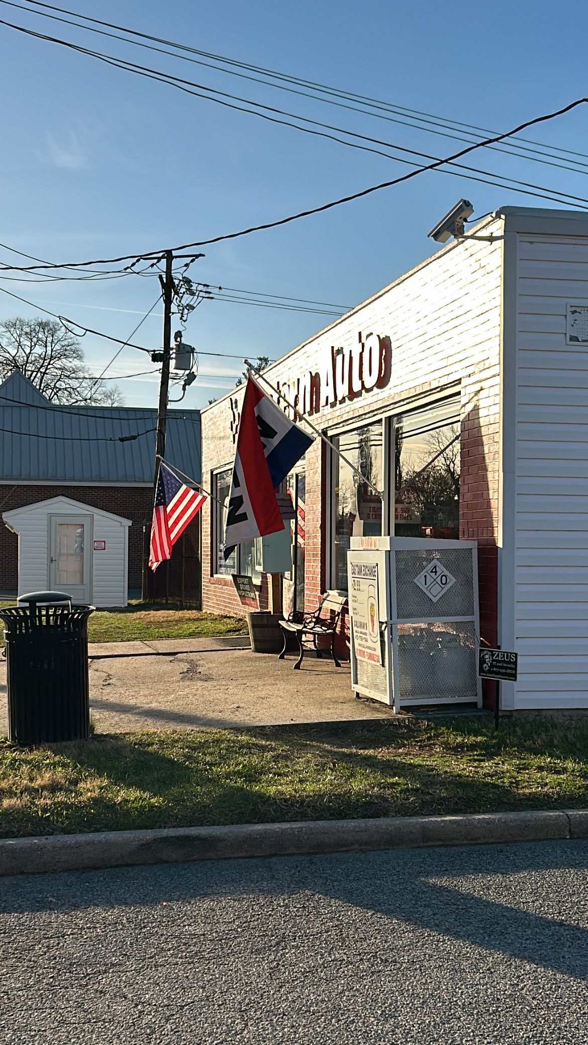 Small white building with flags, including American, under a blue sky | Western Tire & Auto of Centreville