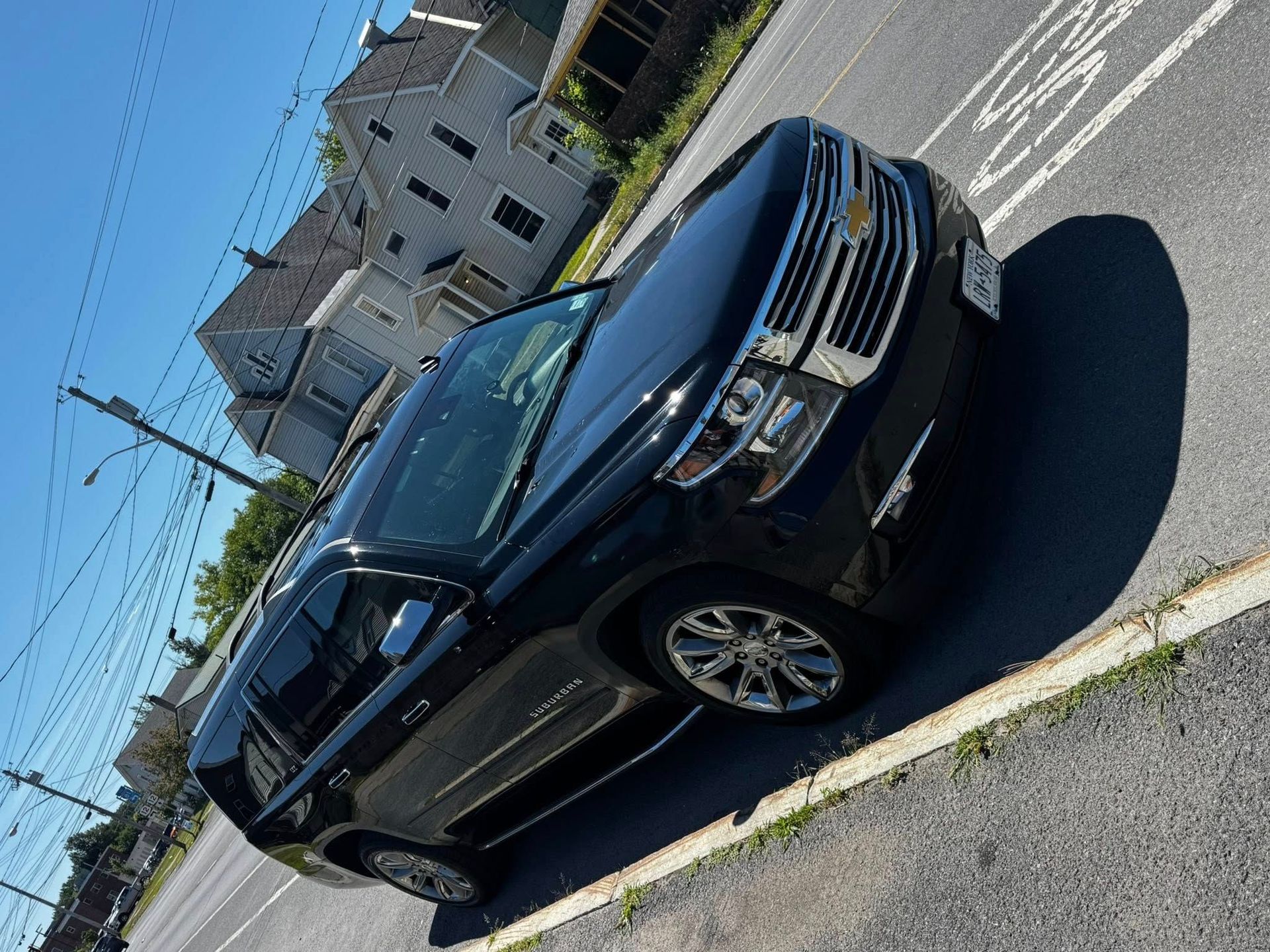 A black Chevrolet Tahoe SUV parked on an asphalt lot in front of houses on a sunny day.