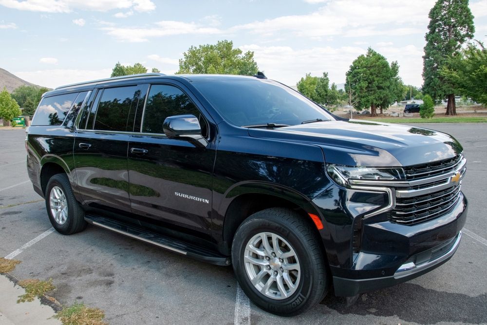 Black Chevrolet Suburban SUV parked in a paved lot under a blue sky.