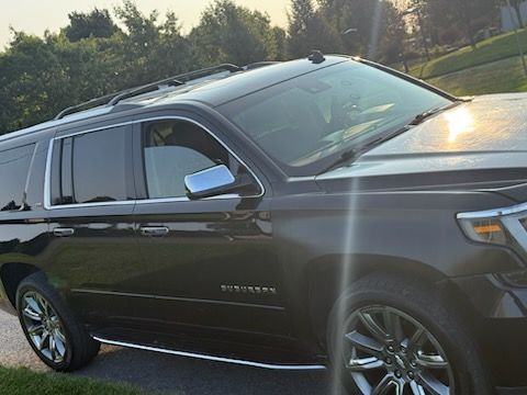 A black Chevrolet Suburban SUV parked on a paved road during a bright, sunny day.