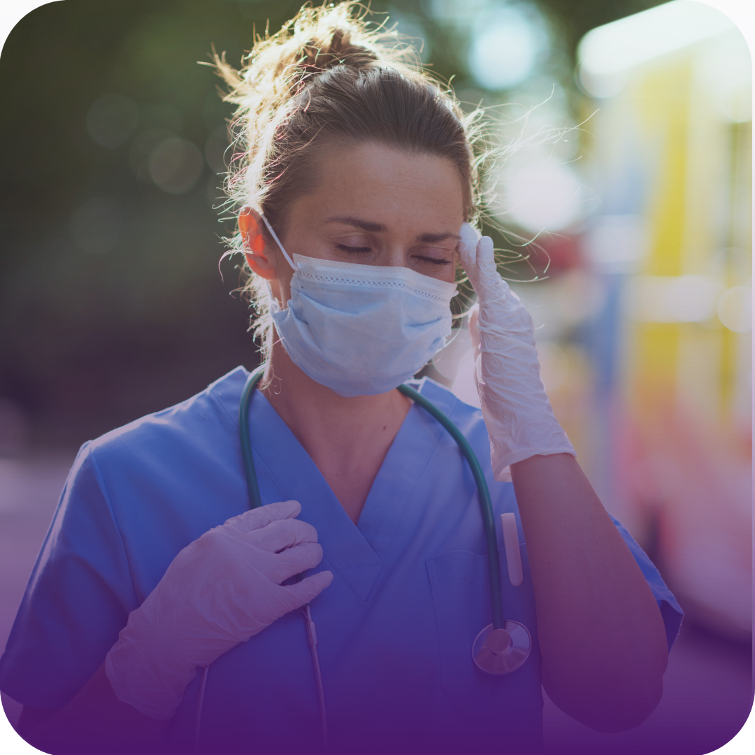 Nurse in scrubs and mask with a stethoscope, touching forehead outside near ambulance.