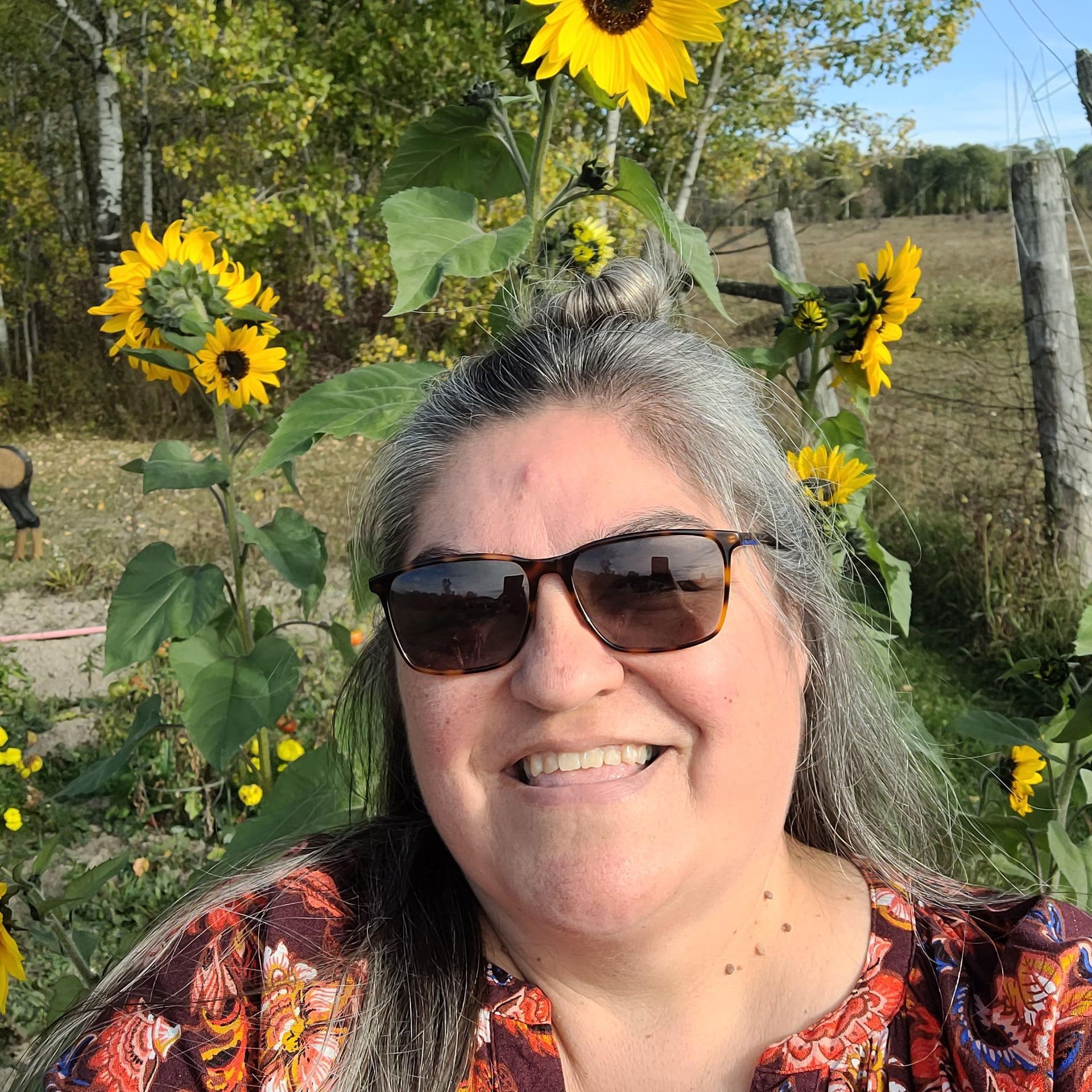 Smiling person wearing sunglasses in a sunflower garden on a sunny day