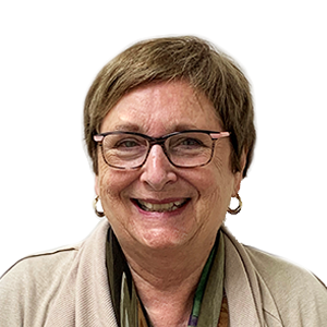 Woman with glasses smiles; tan sweater, short brown hair.