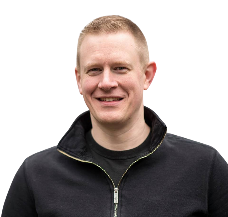 Man with short blonde hair smiles, wearing a black zip-up jacket.