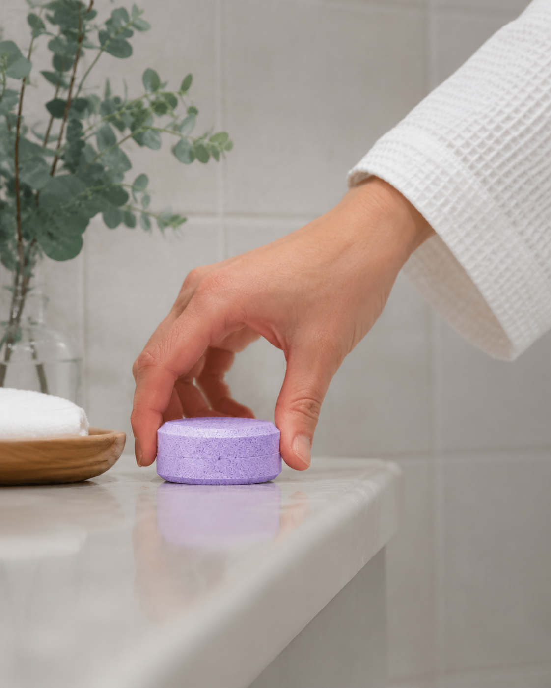 Hand placing a purple soap bar on a bathroom counter near a sink