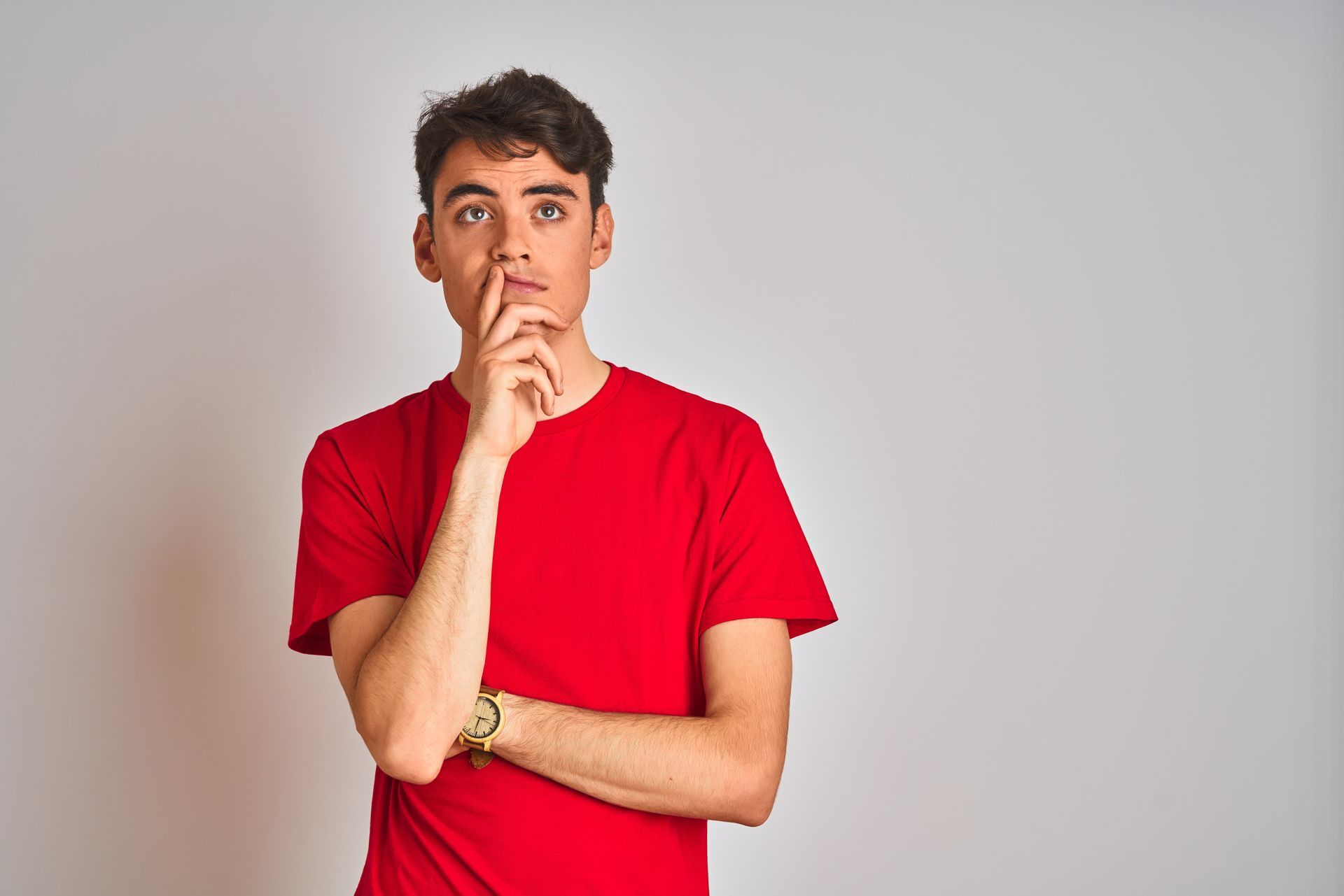 Person in a red t-shirt, hand on chin, looking upward, appears to be thinking. Against a white backdrop.