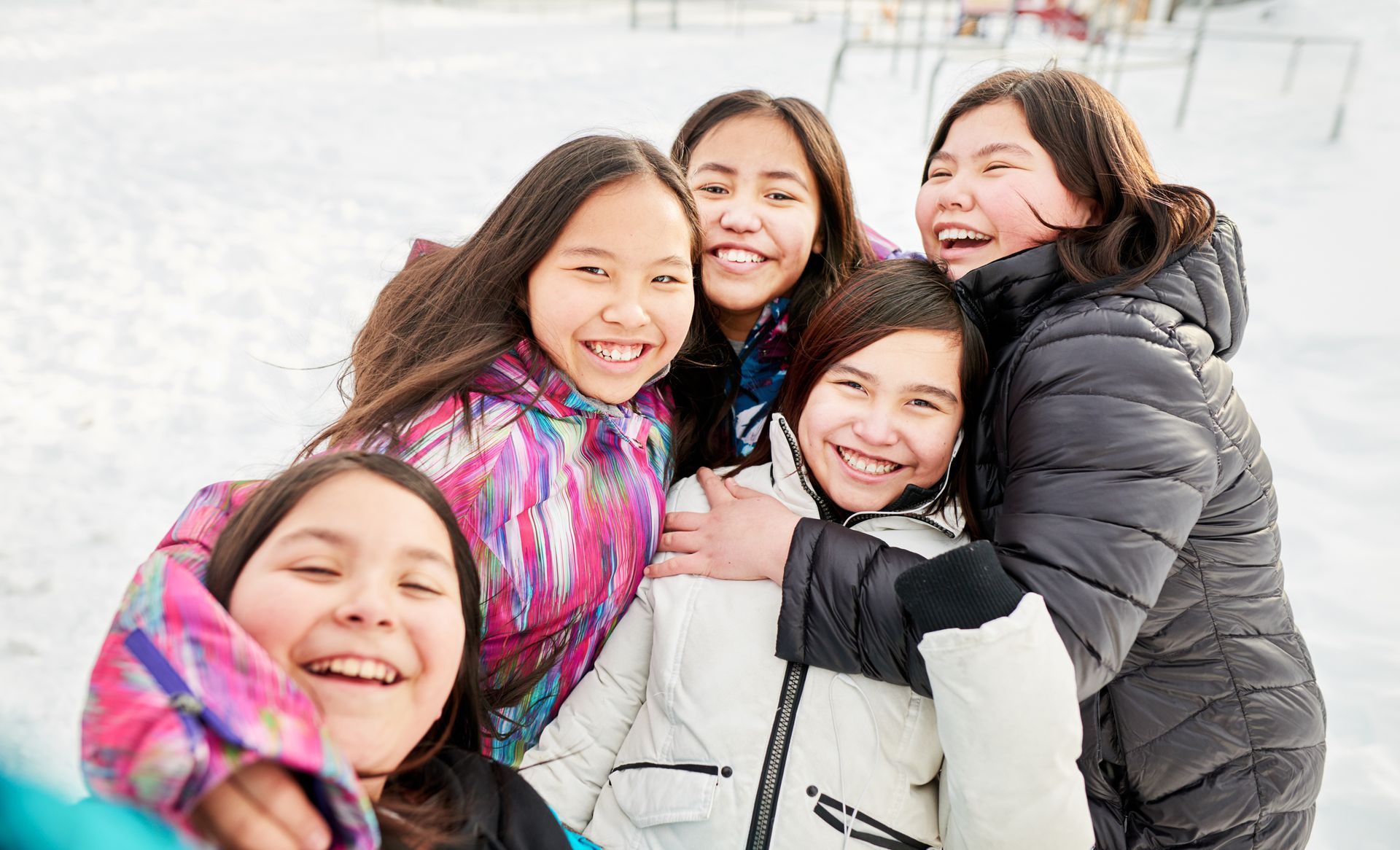 Group of smiling girls huddled together outdoors in snowy setting.