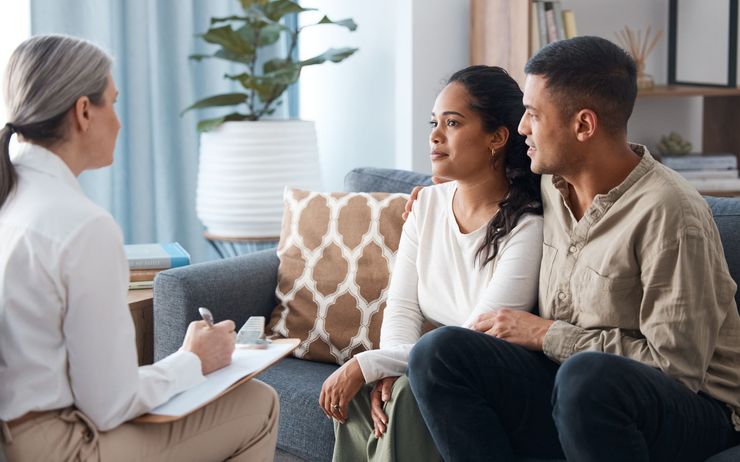 Couple consulting with a therapist, sitting on a sofa. Therapist takes notes.