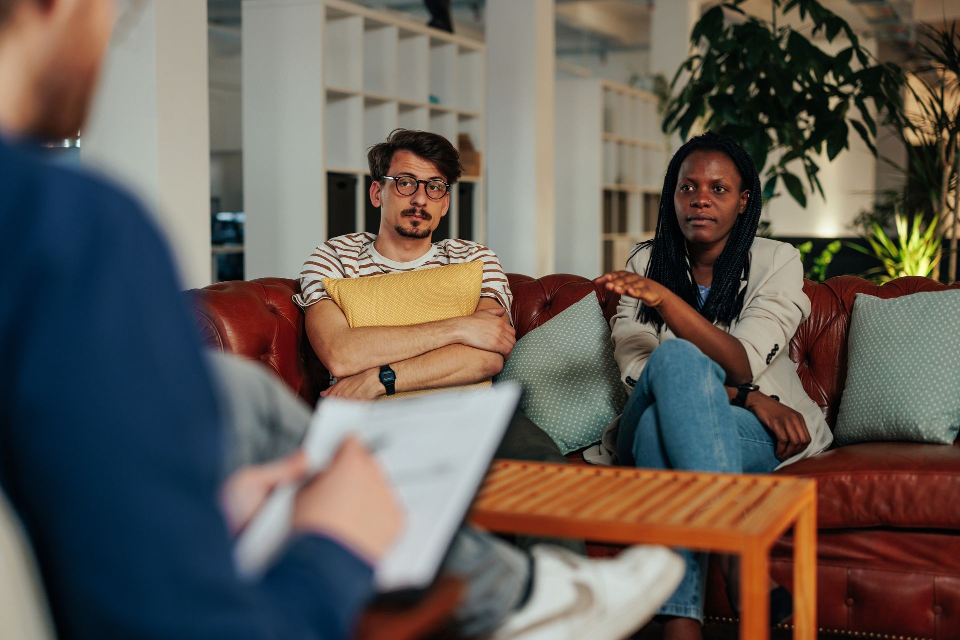Couple in therapy session, sitting on a red couch, talking to therapist.
