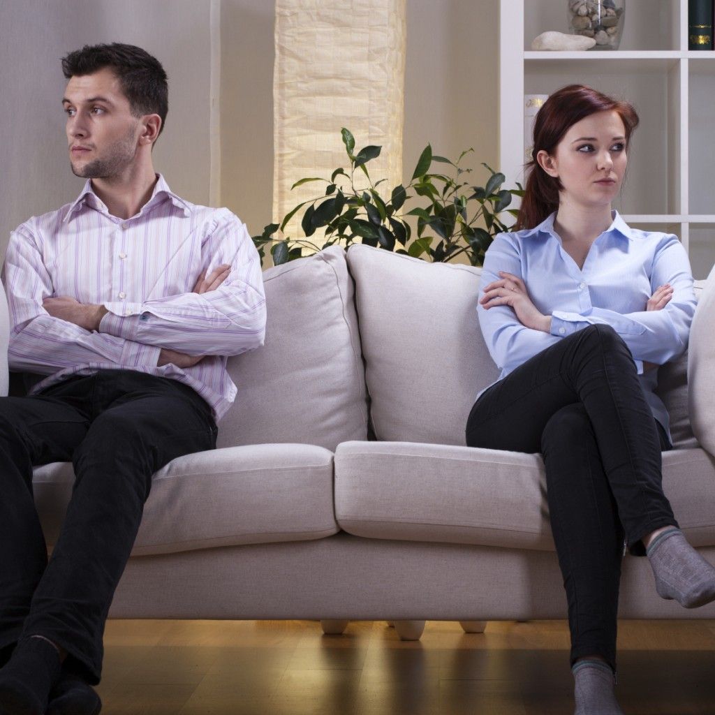 Man and woman on a couch, arms crossed, looking away from each other.