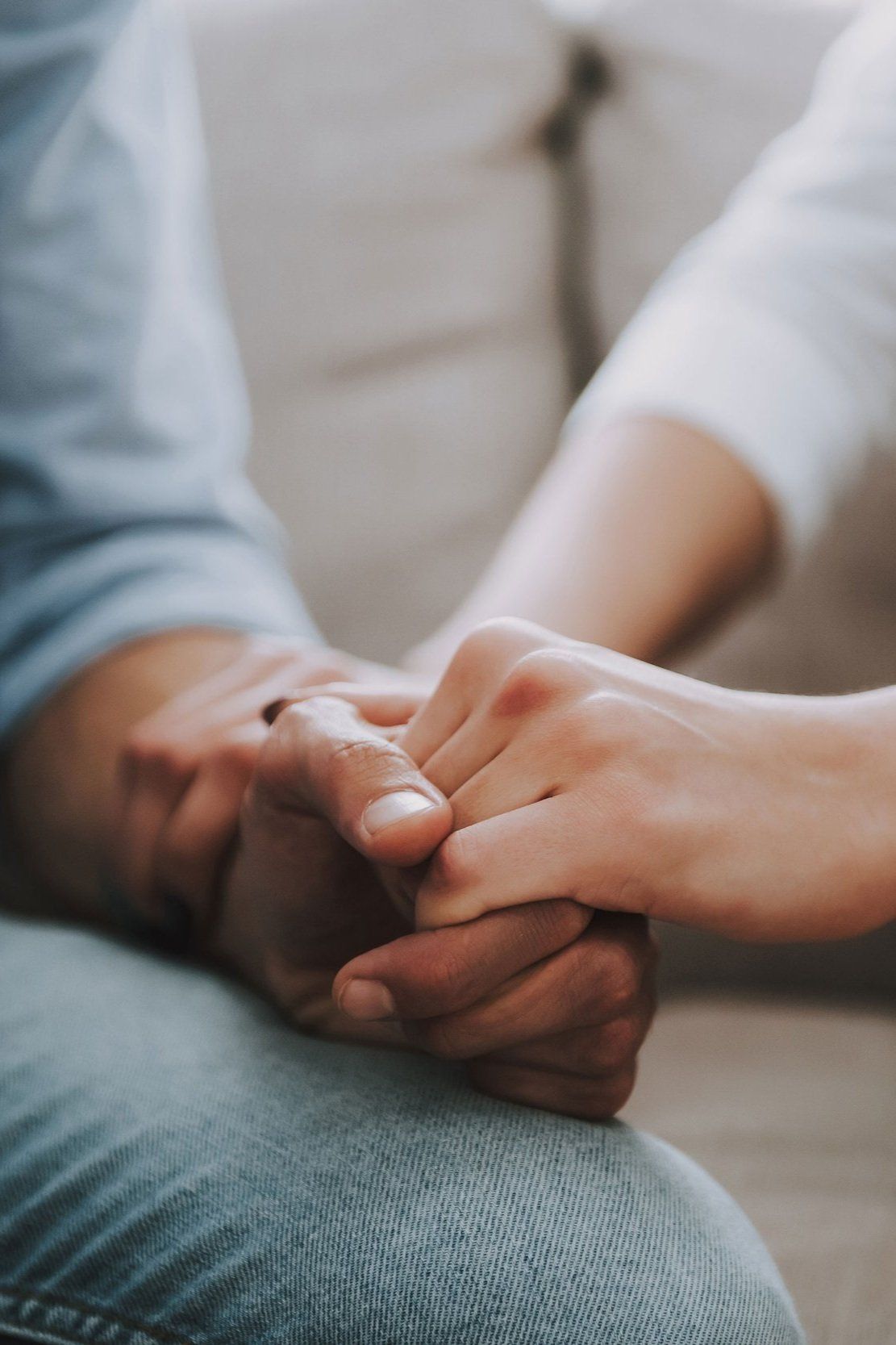 Hands clasped in comfort; one hand rests over the other, light colors, indoors.