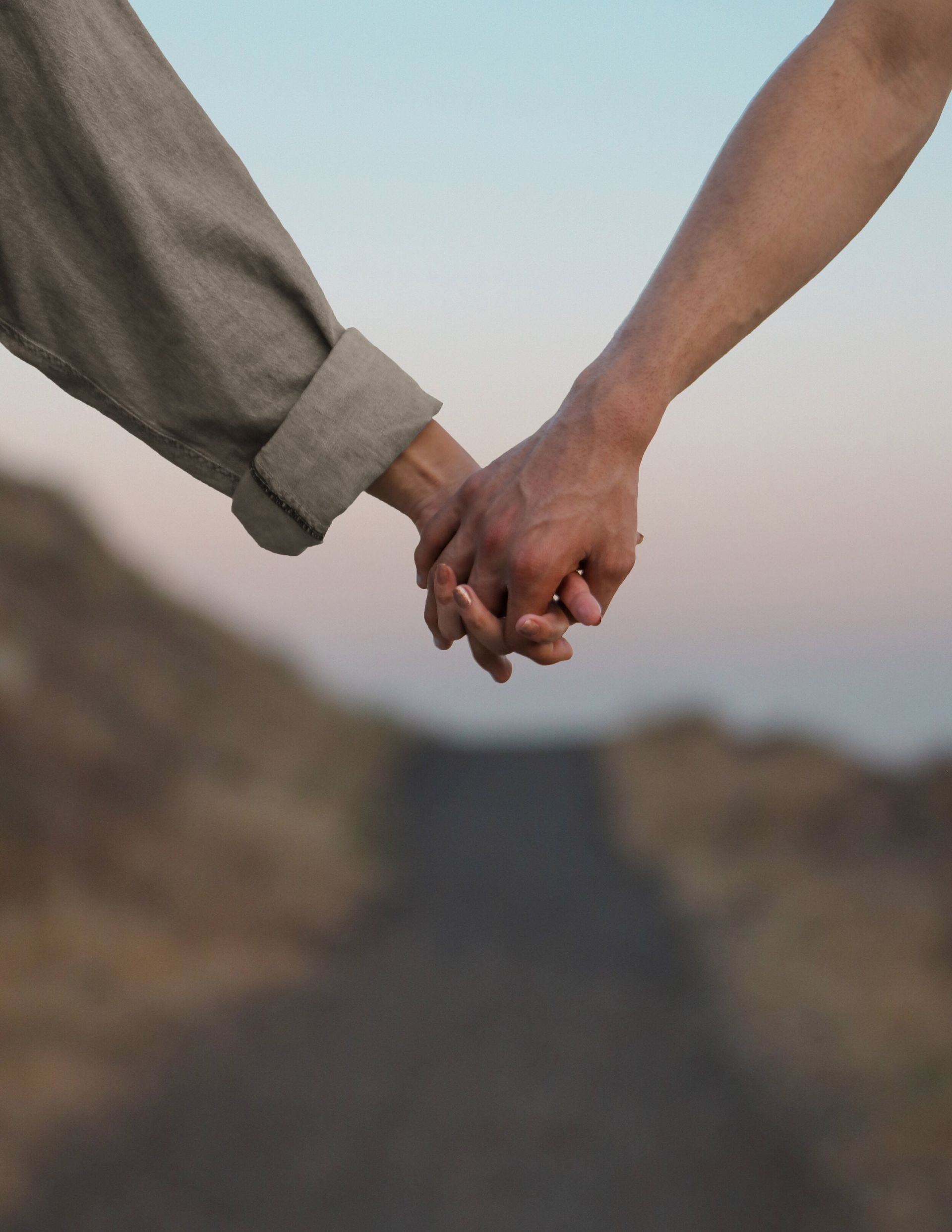 Two hands holding each other tightly, the background is a blurred road with a light sky.