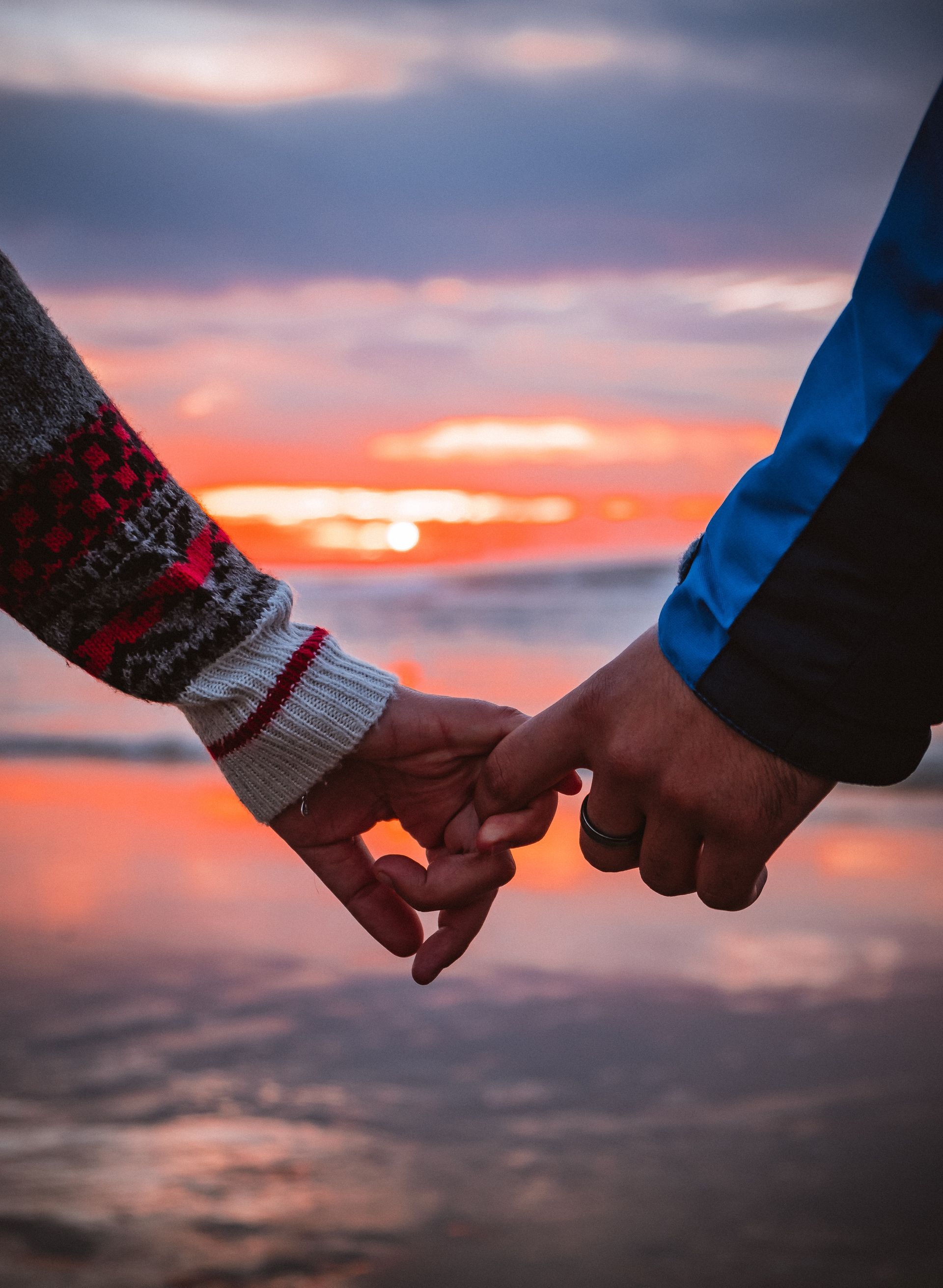 Two people holding hands, sunset sky in background.