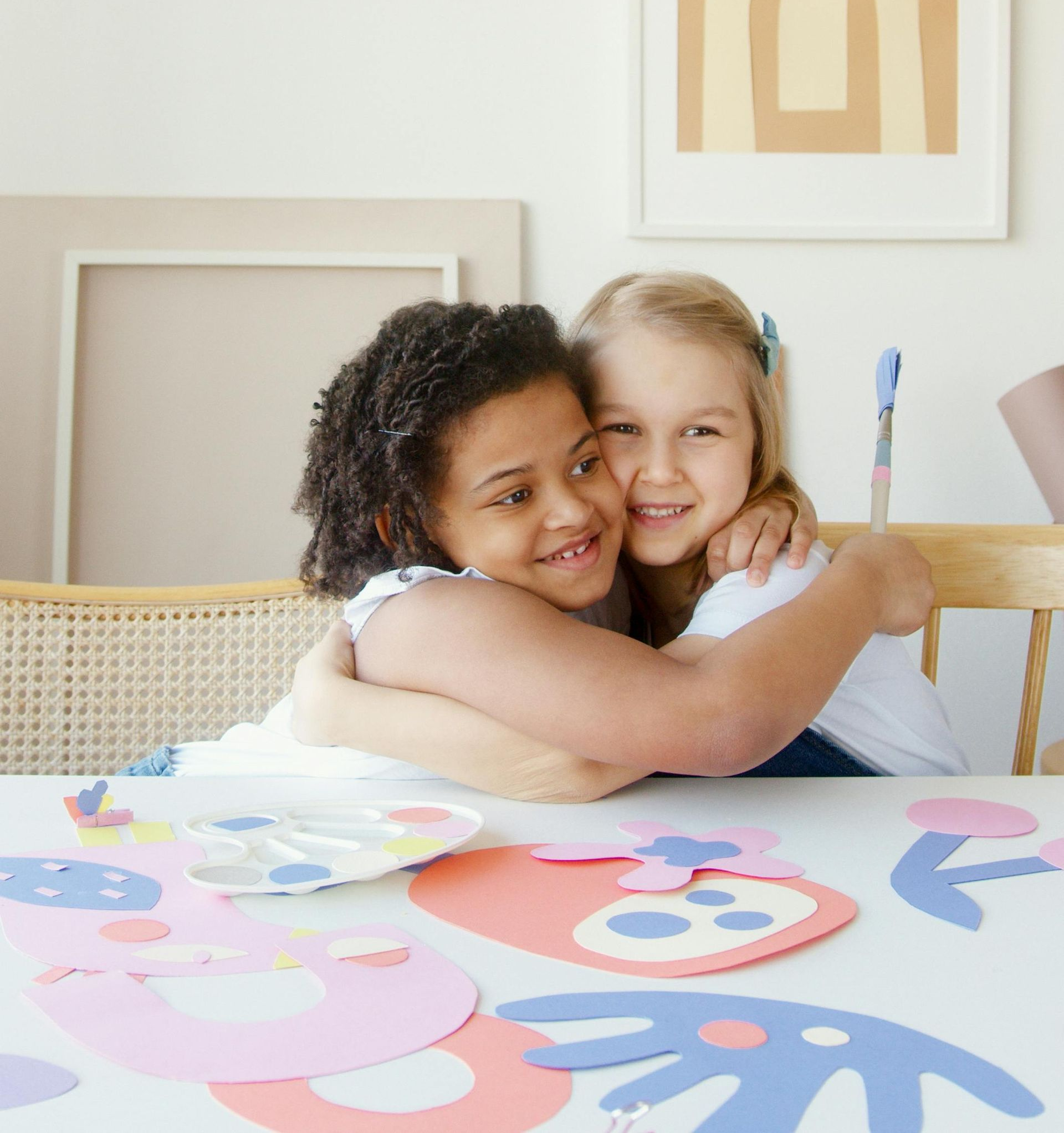 Two smiling children hugging at a table with craft supplies.