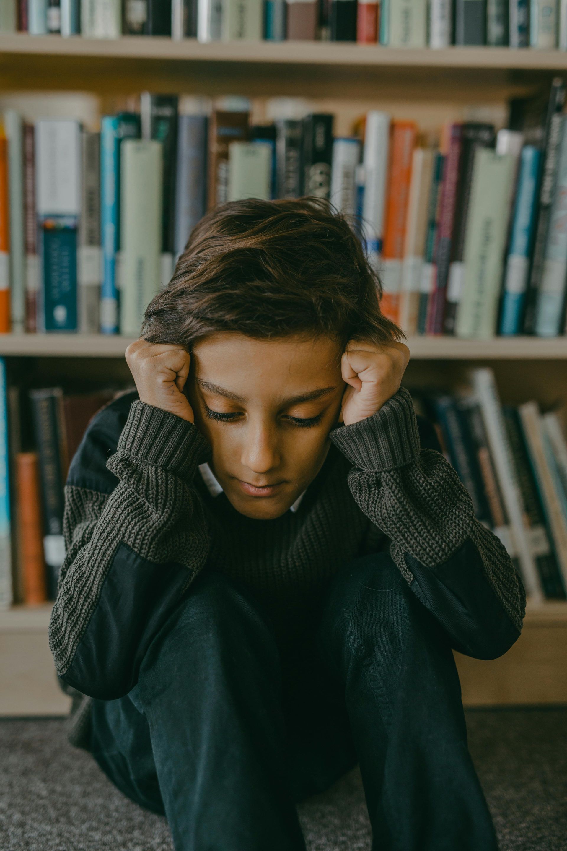 Boy sitting, head in hands, in front of a bookcase.