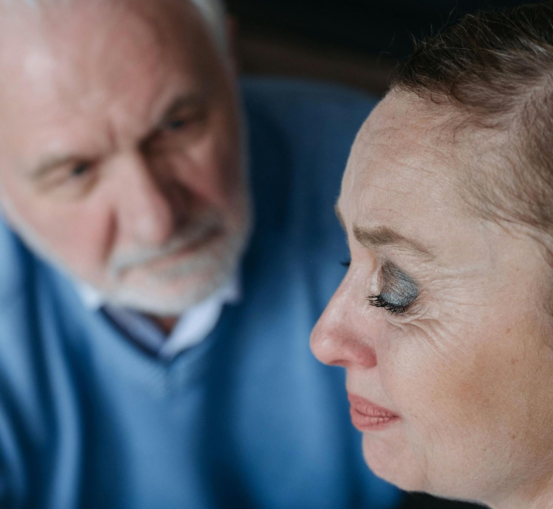 Woman with smudged makeup looking down, man behind with concerned expression.