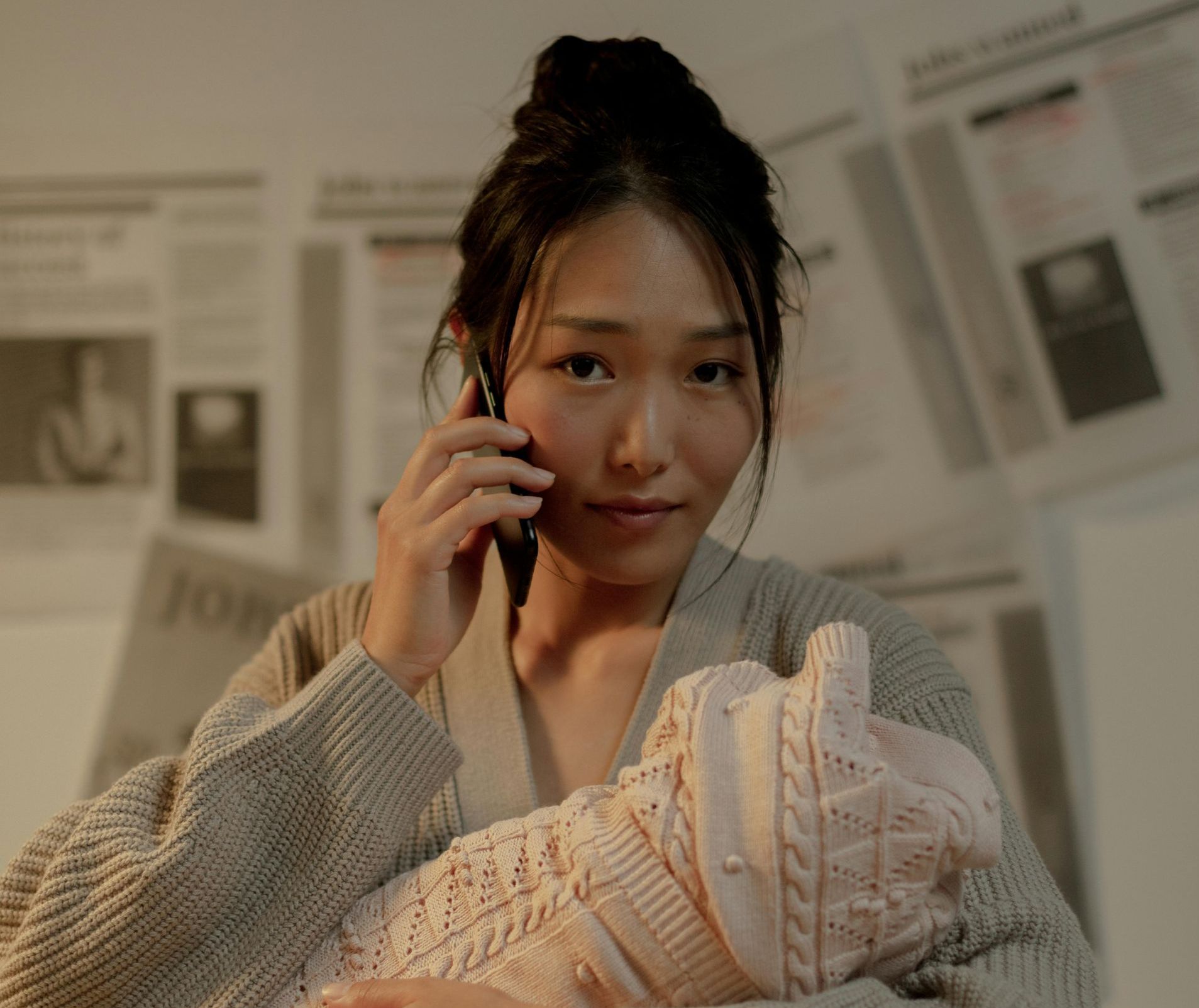 Woman holding baby, talking on phone, surrounded by newsprint.