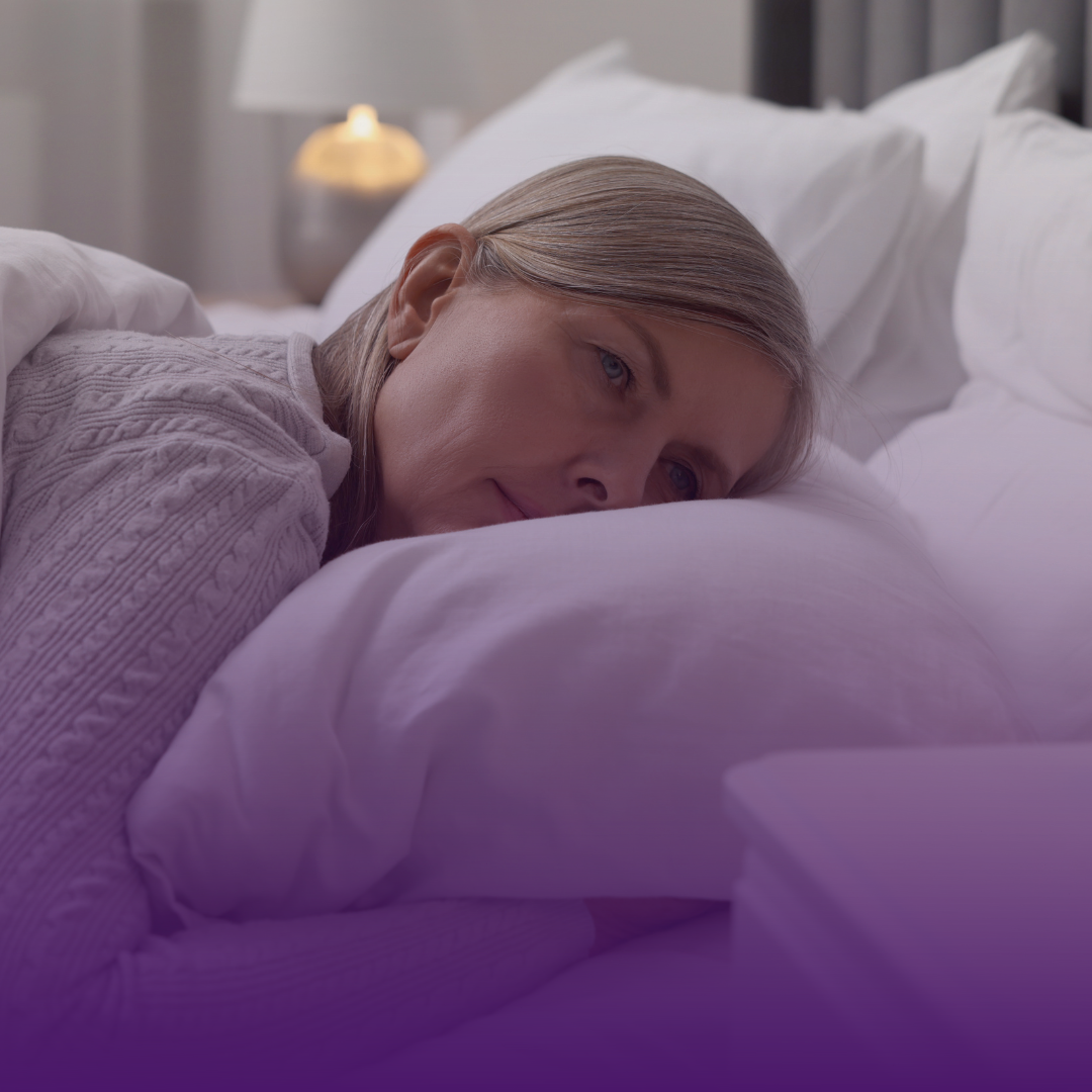 Woman lying in bed, resting head on pillow. Bedroom setting with lamp and nightstand.