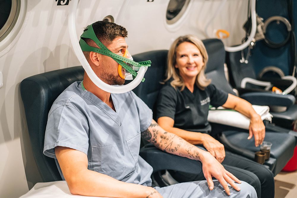 A man wearing an oxygen mask is sitting in a chair next to a woman.