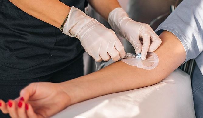 Medical professional inserting an IV needle into a patient's arm, indoors.