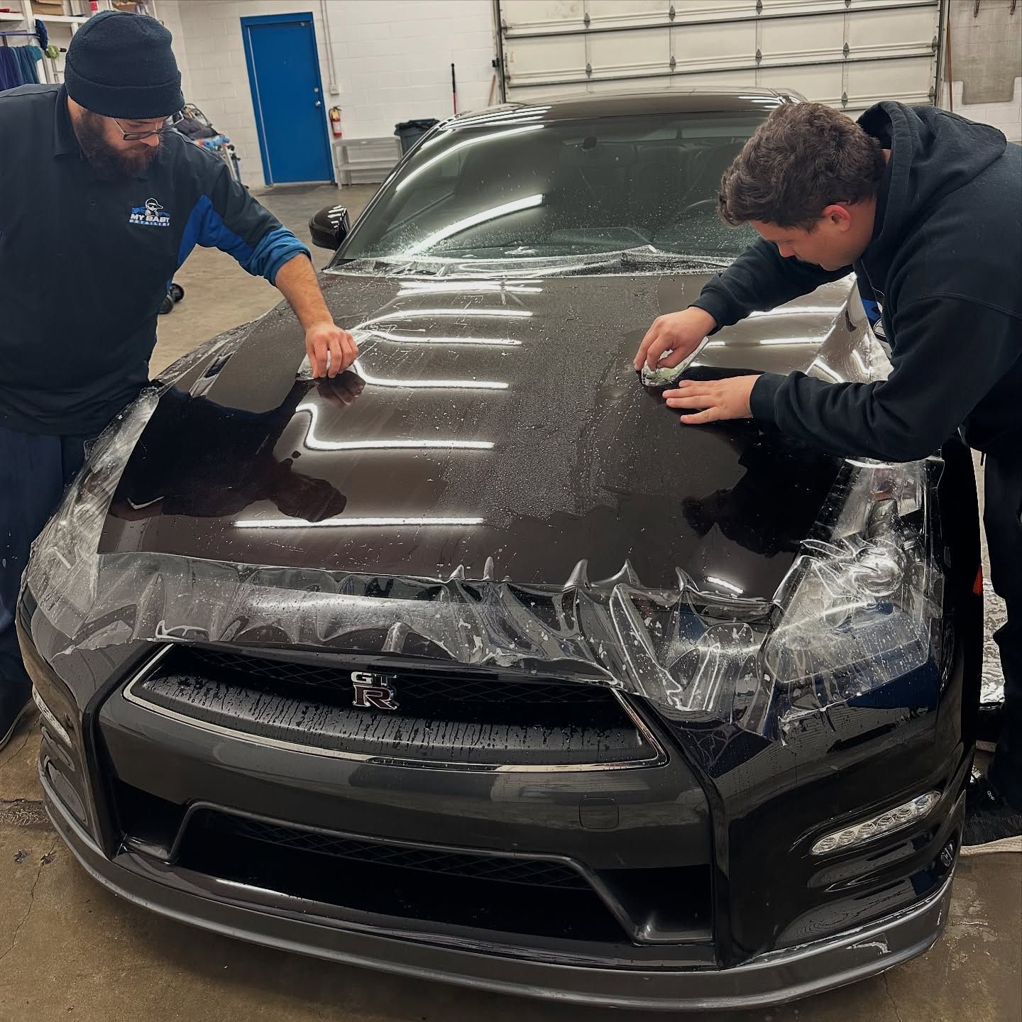 A person wearing black gloves working on a blue car, possibly applying a decal.