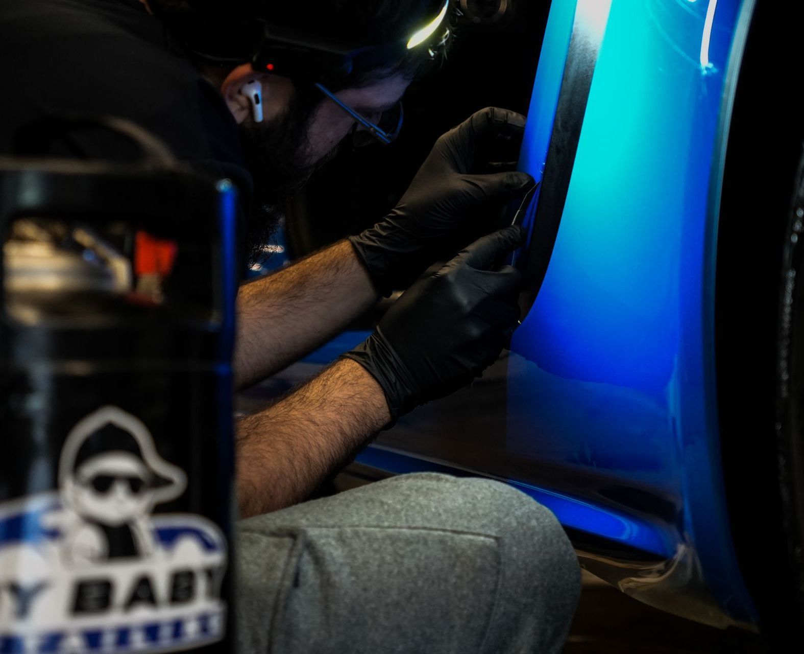A person wearing black gloves working on a blue car, possibly applying a decal.