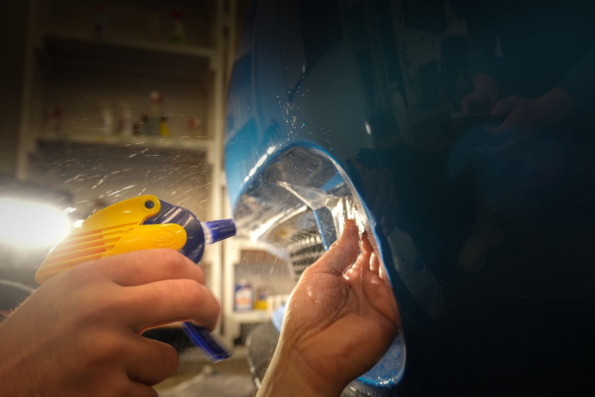 Person rinsing a blue car headlight with water.