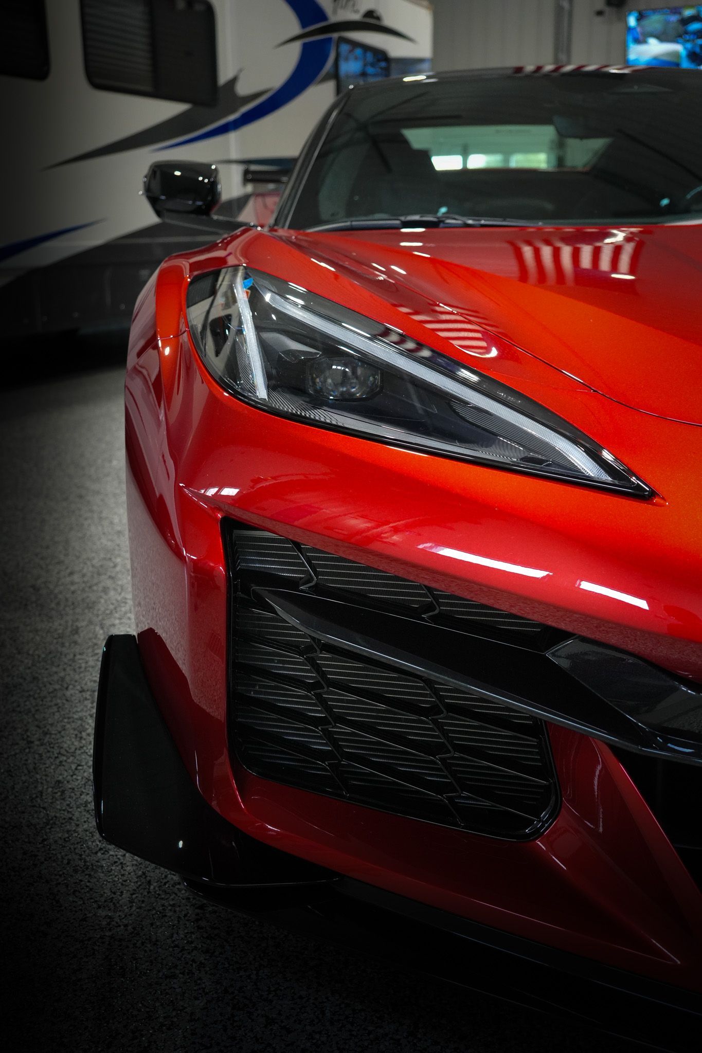 A red sports car is parked in a garage with a trailer in the background.