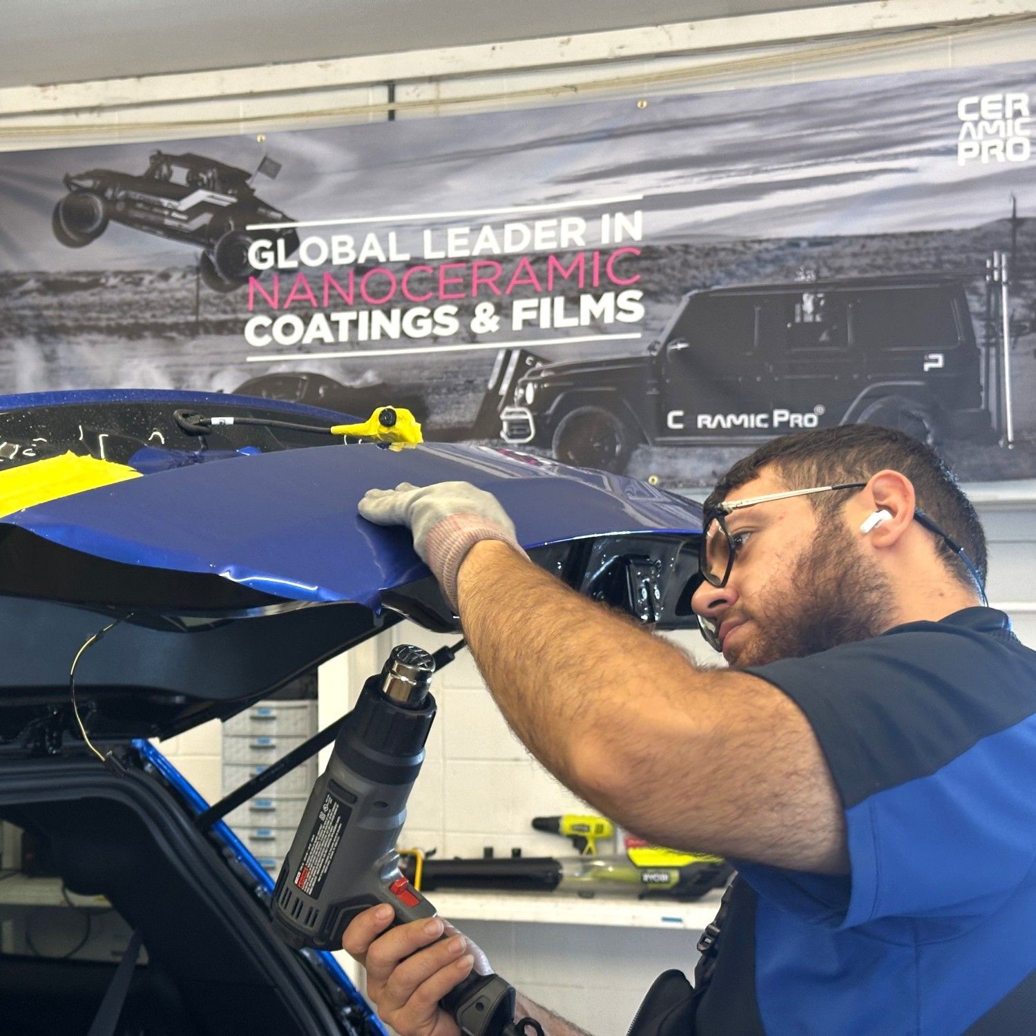 Technician applying blue film to a car panel in an auto shop