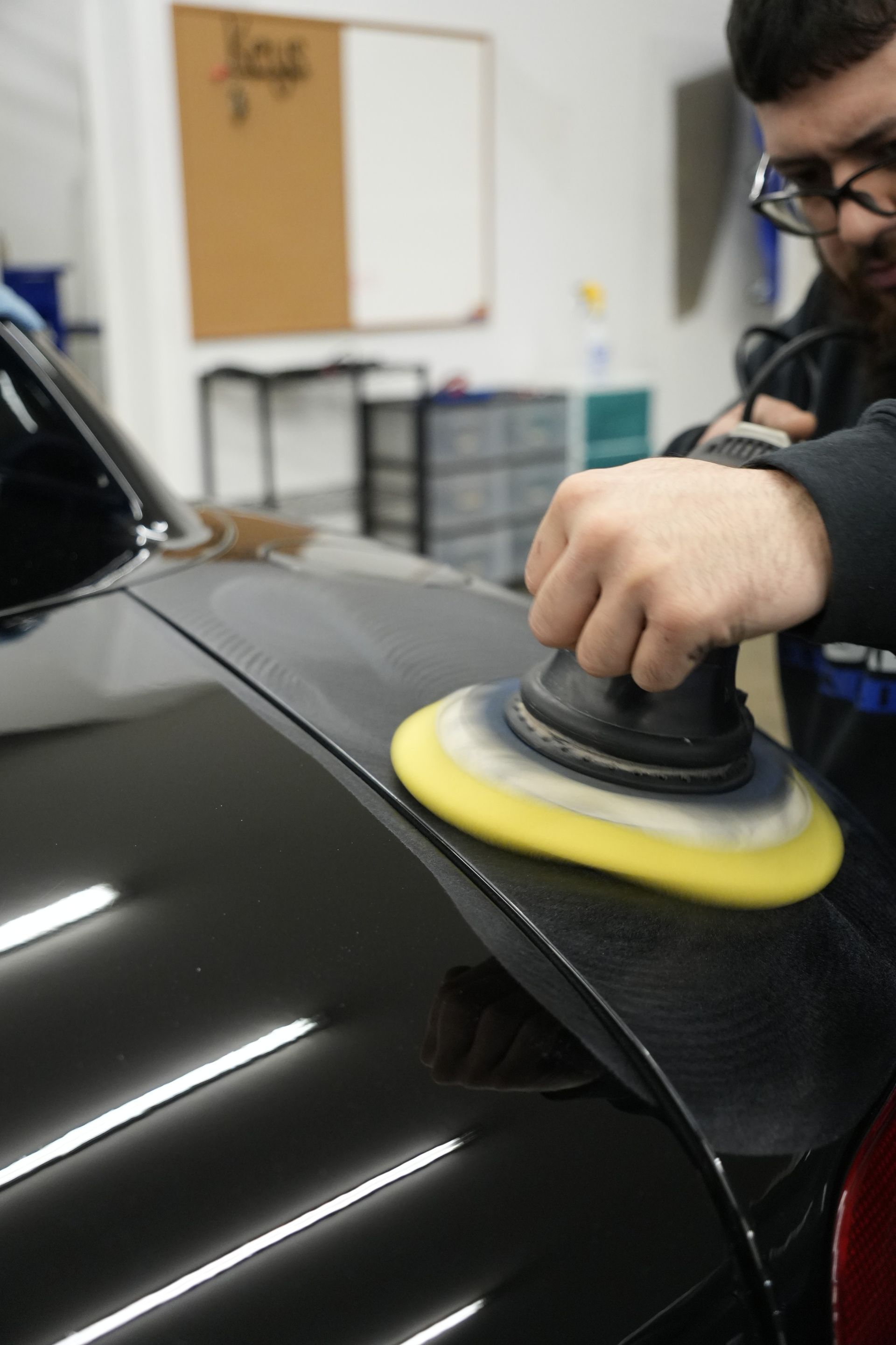 A man is polishing a red car in a garage.