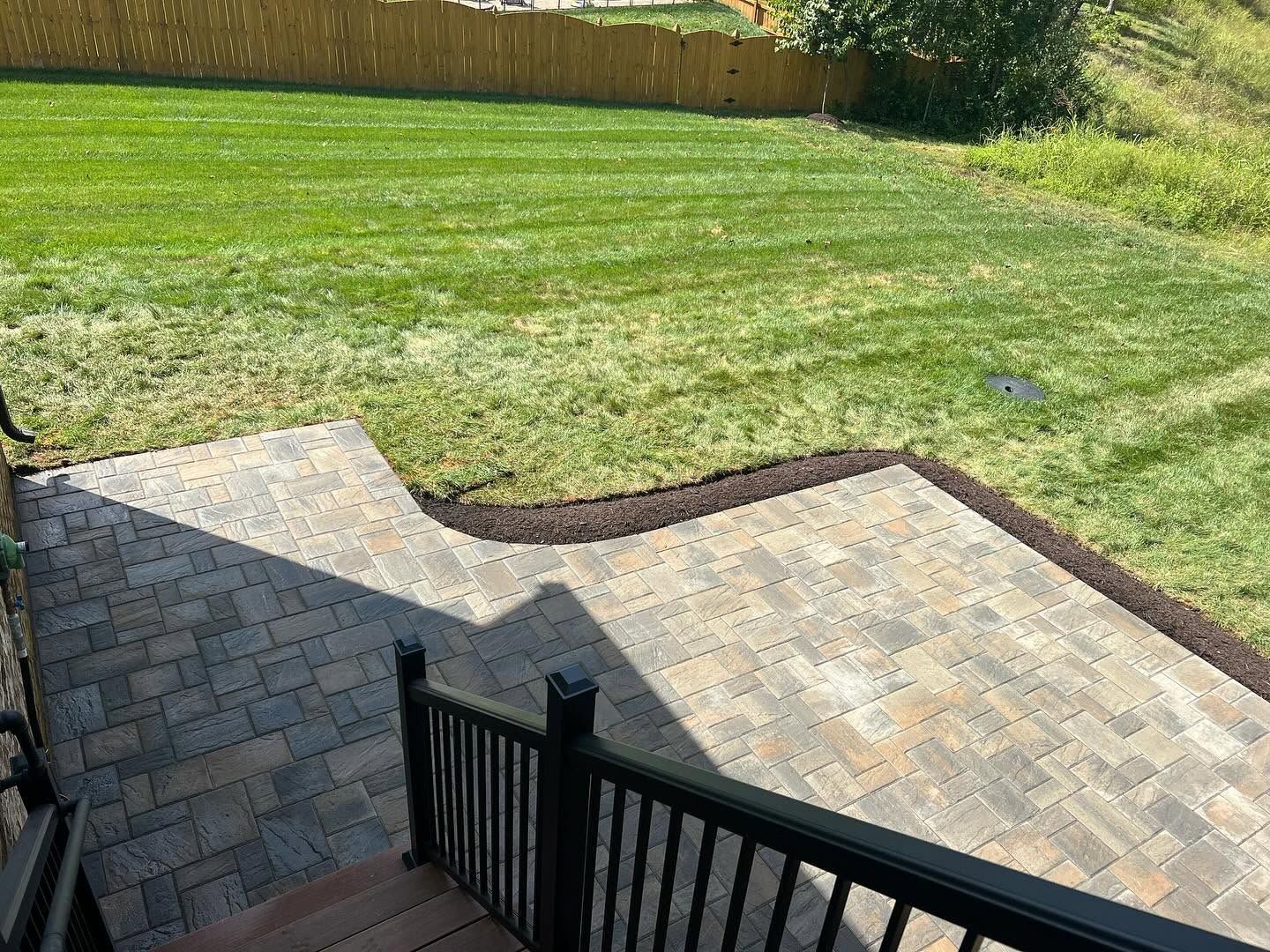 A narrow white-rock garden bed with small plants runs alongside a screened patio and green lawn.